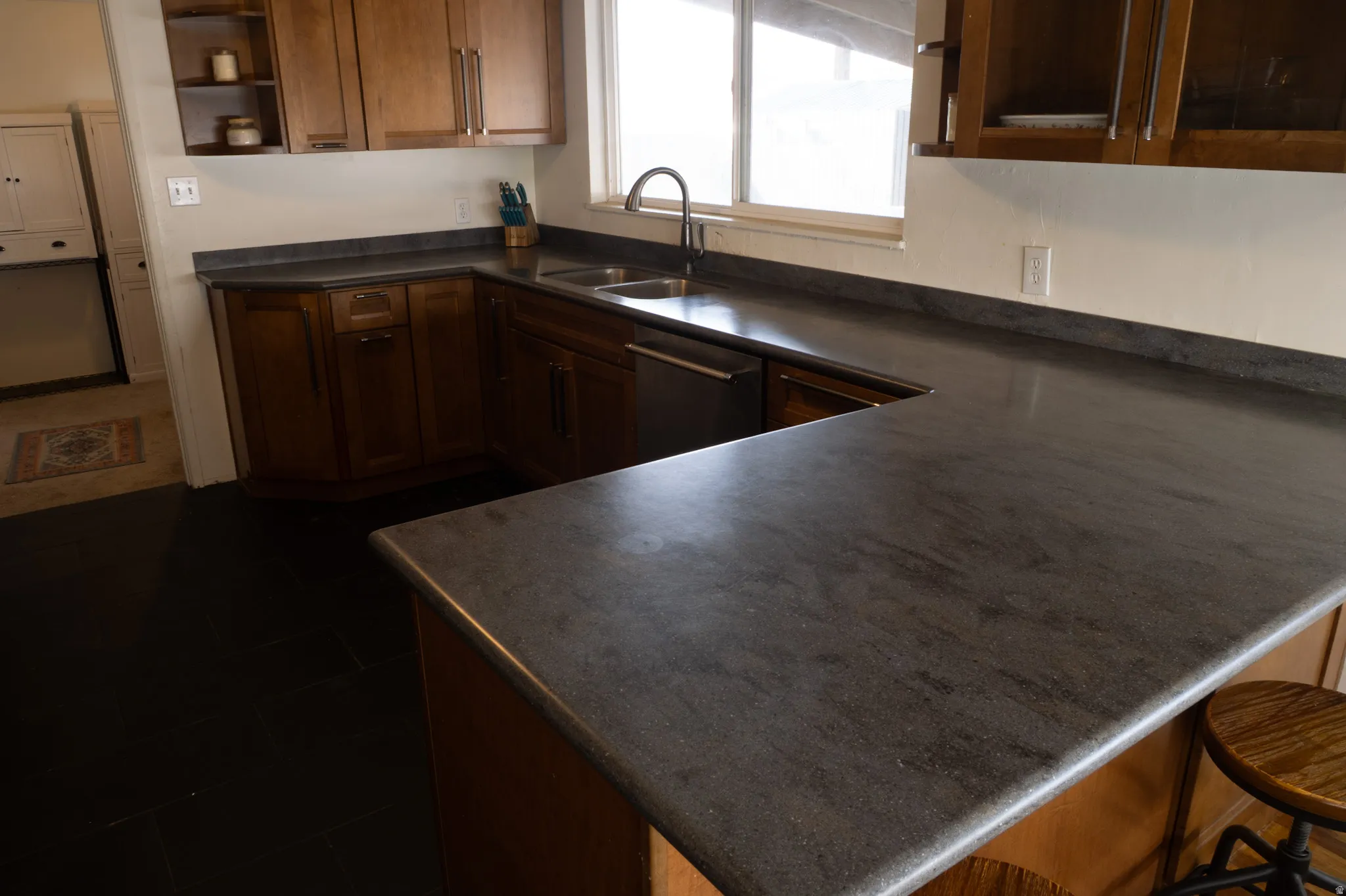 Kitchen with dark countertops, open shelves, a peninsula, dishwasher, and a breakfast bar area