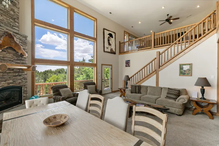 Carpeted dining room featuring a ceiling fan, a stone fireplace, and a high ceiling