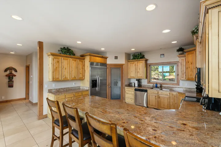 Kitchen featuring a peninsula, black appliances, a breakfast bar, light stone counters, and light wood finish cabinetry