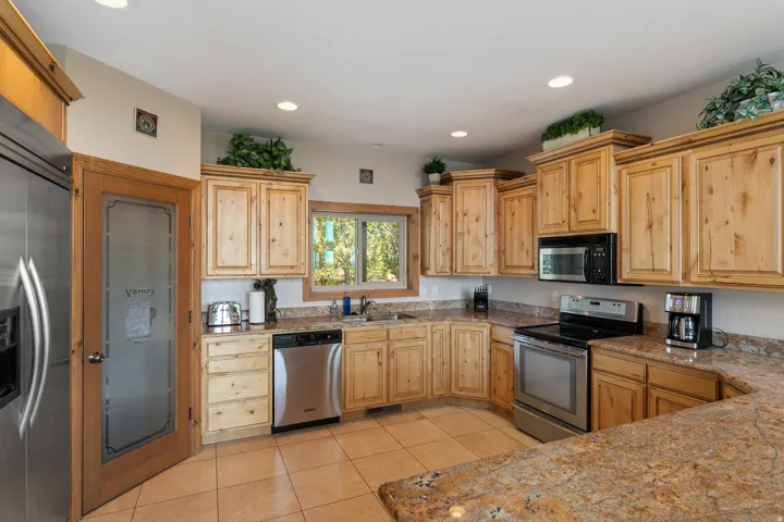 Kitchen with stainless steel appliances, light tile patterned flooring, light wood finish cabinets, recessed lighting, and light stone counters