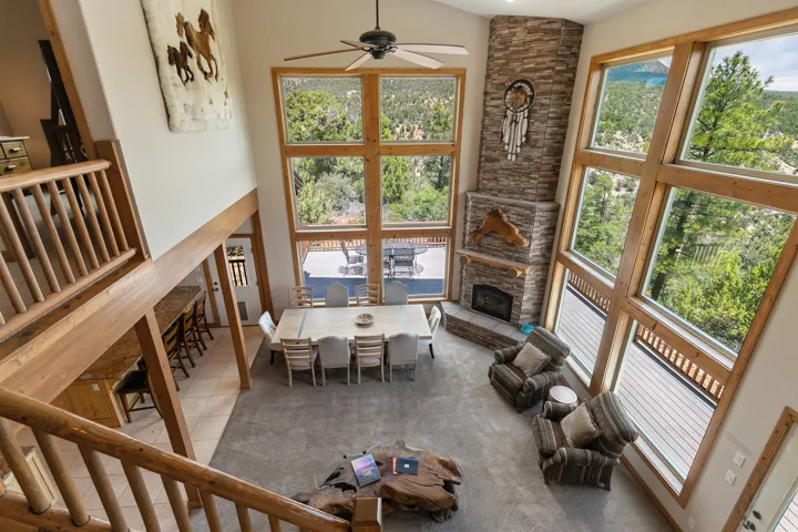 Tiled living area with a ceiling fan, a stone fireplace, vaulted ceiling, and plenty of natural light