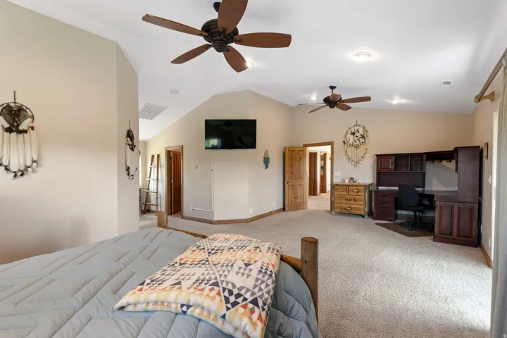 Carpeted bedroom with a desk, lofted ceiling, and a ceiling fan