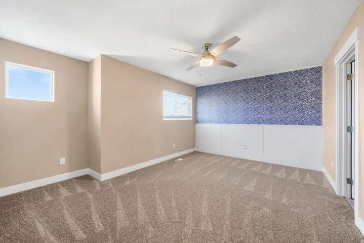 Primary bedroom wallpapered and wainscoted accent wall, and ceiling fan