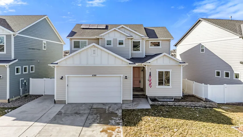 View of front of property featuring board and batten siding, solar panels, a shingled roof, and concrete driveway