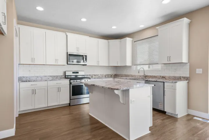 Kitchen featuring white cabinetry, stainless steel appliances, a kitchen breakfast bar, light stone countertops, and dark wood-type flooring