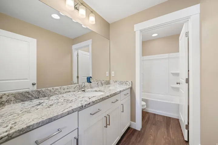 Secondary bathroom featuring vanity with granite counters, dark wood-type flooring, shower / tub combination, and recessed lighting