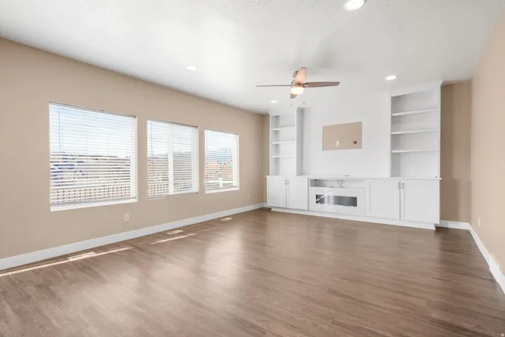 Unfurnished living room featuring dark wood laminate floors, a ceiling fan, recessed lighting, a textured ceiling, and built in features