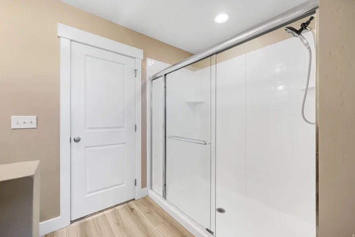 Primary en-suite bathroom with a walk-in shower, light wood-type flooring, and recessed lighting