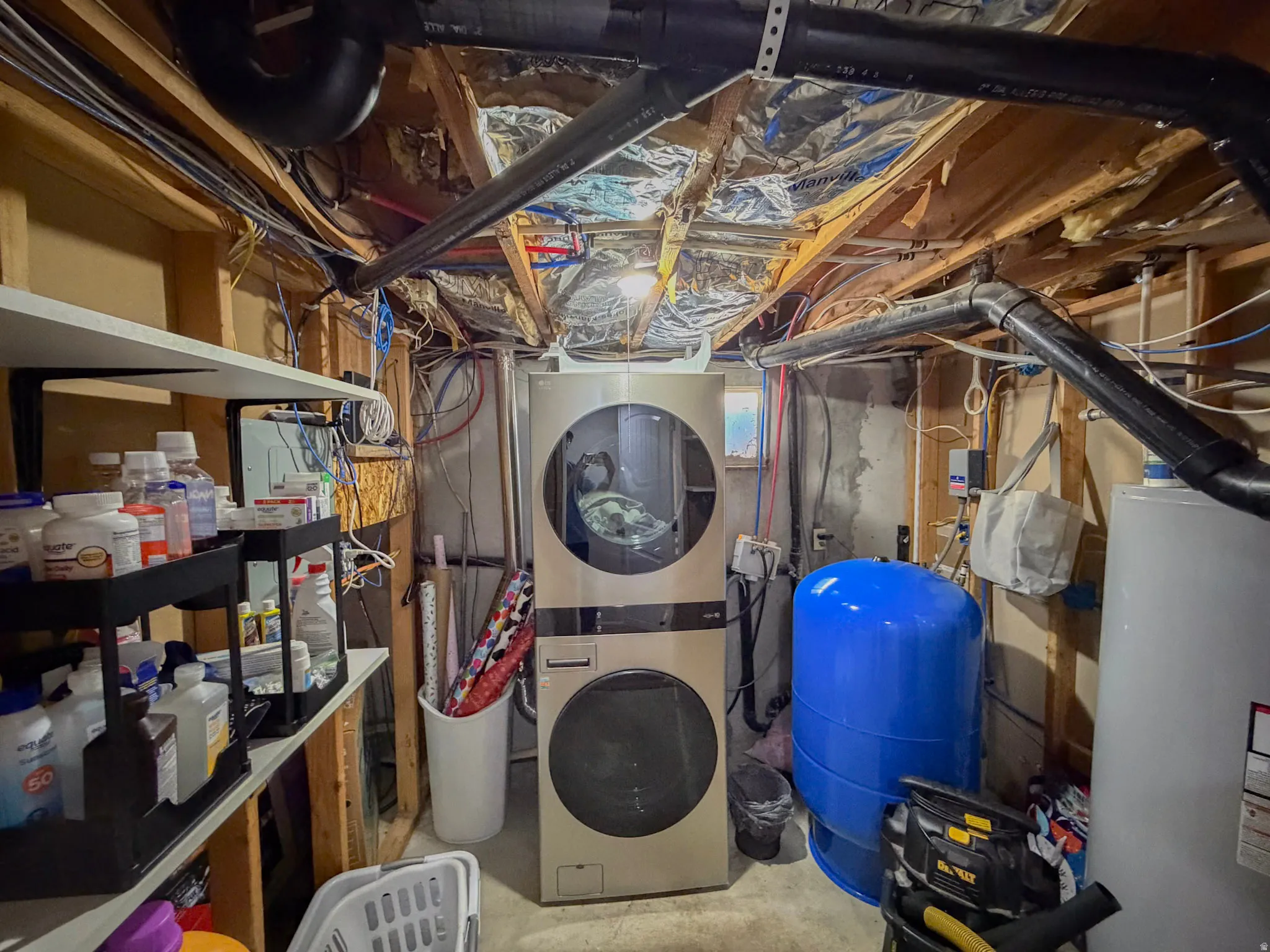 Unfinished basement with a water pressure tank, stacked washer / drying machine, and water heater