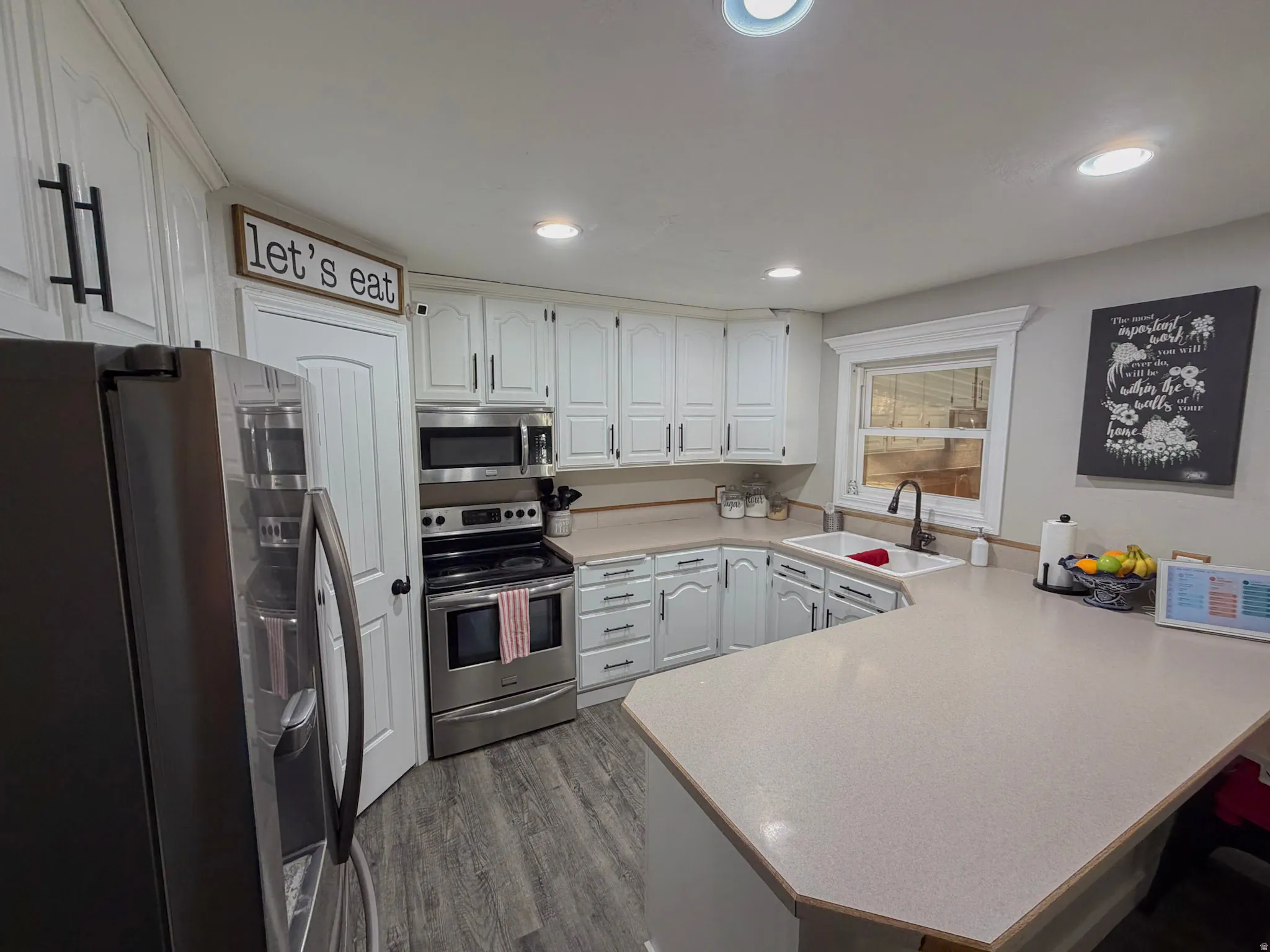 Kitchen featuring stainless steel appliances, light countertops, a peninsula, white cabinetry, and dark wood-type flooring