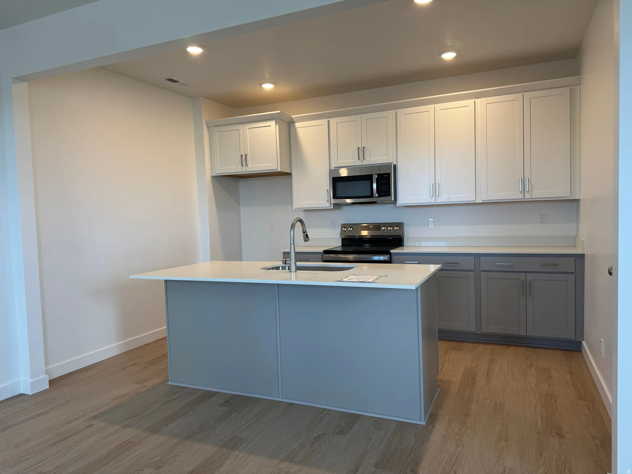 Kitchen with stainless steel appliances, recessed lighting, dark wood-style floors, two tone cabinets, and a center island with sink