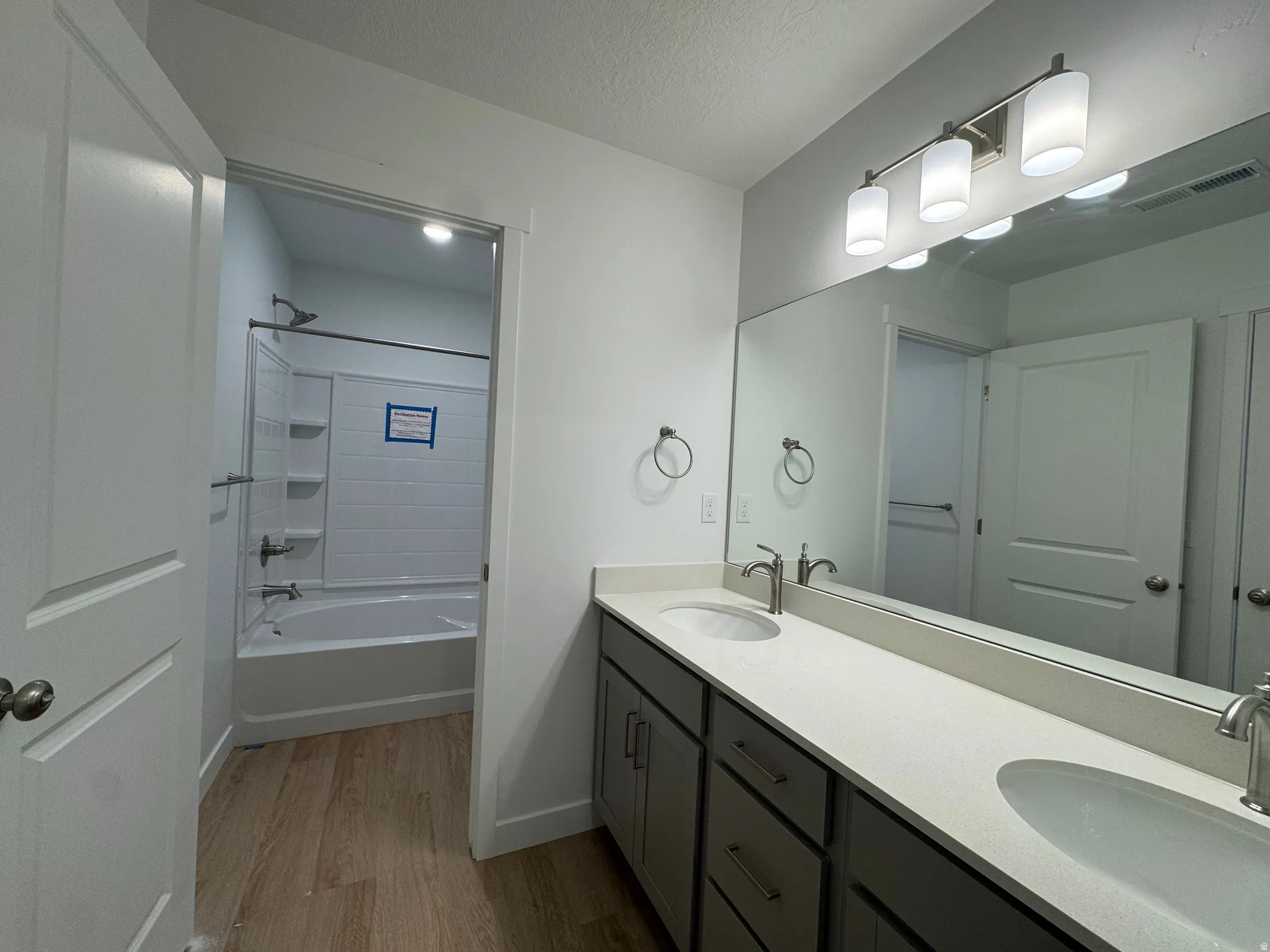 Full bathroom featuring double vanity, shower / bathtub combination, light wood-style floors, and a textured ceiling