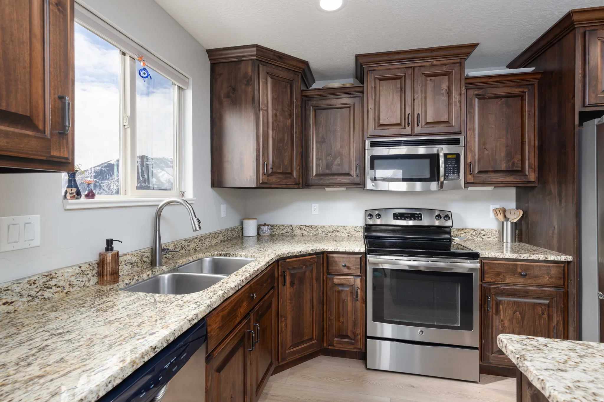 Kitchen with stainless steel appliances, dark wood finish cabinets, and light stone counters