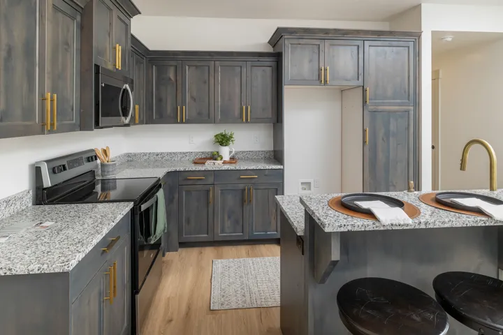 Gray-stained cabinetry with gold-toned hardware, light-toned wood-finish flooring, granite countertops, and a built-in microwave