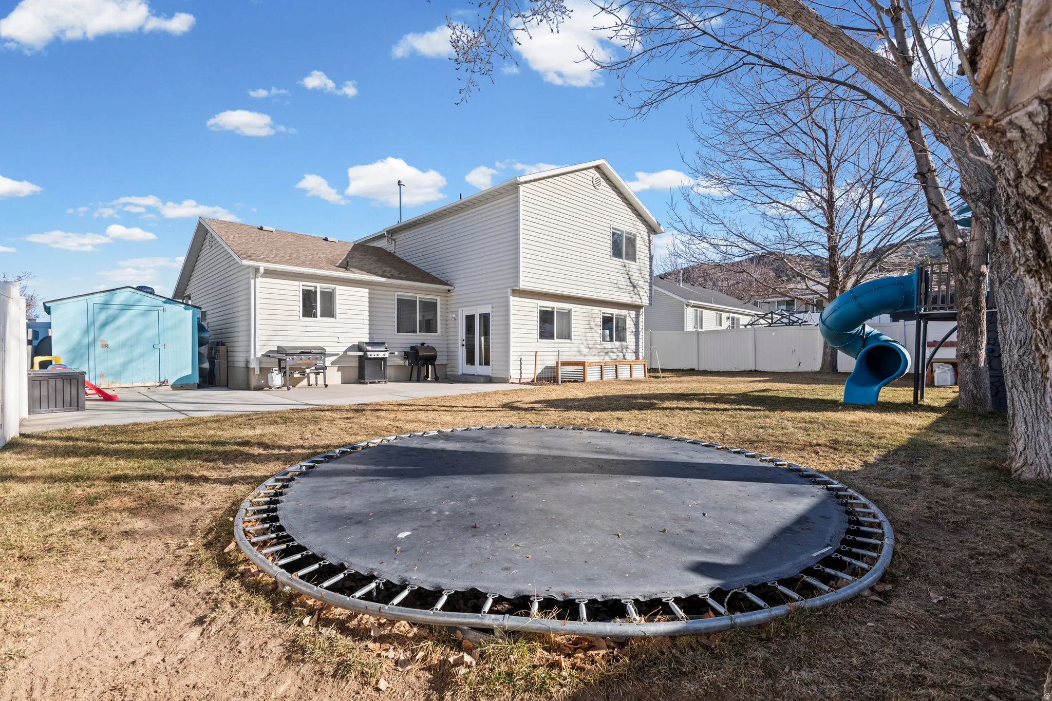 Back of property featuring a storage unit, a playground, a patio, and a trampoline