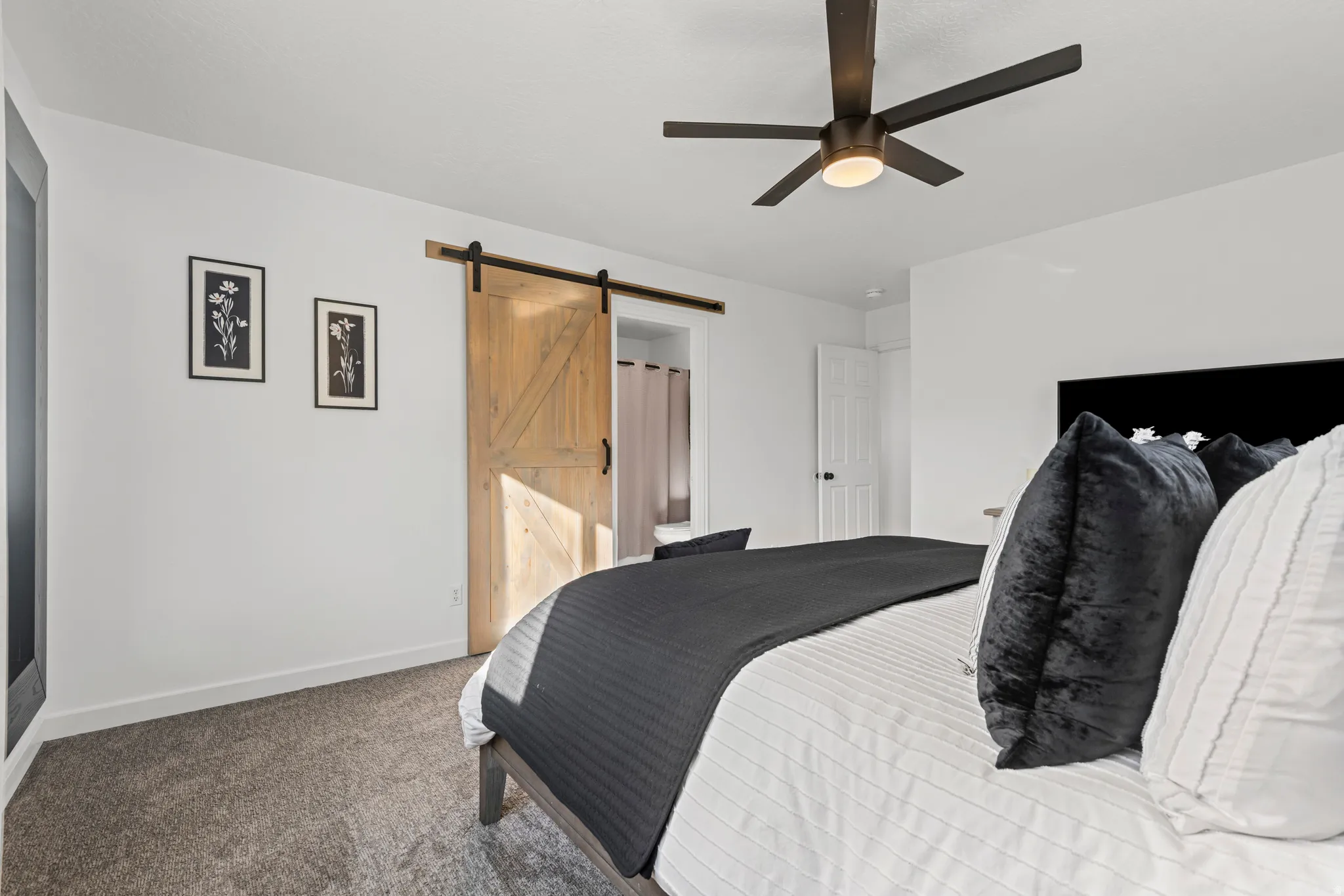 Carpeted bedroom with a barn door and a ceiling fan