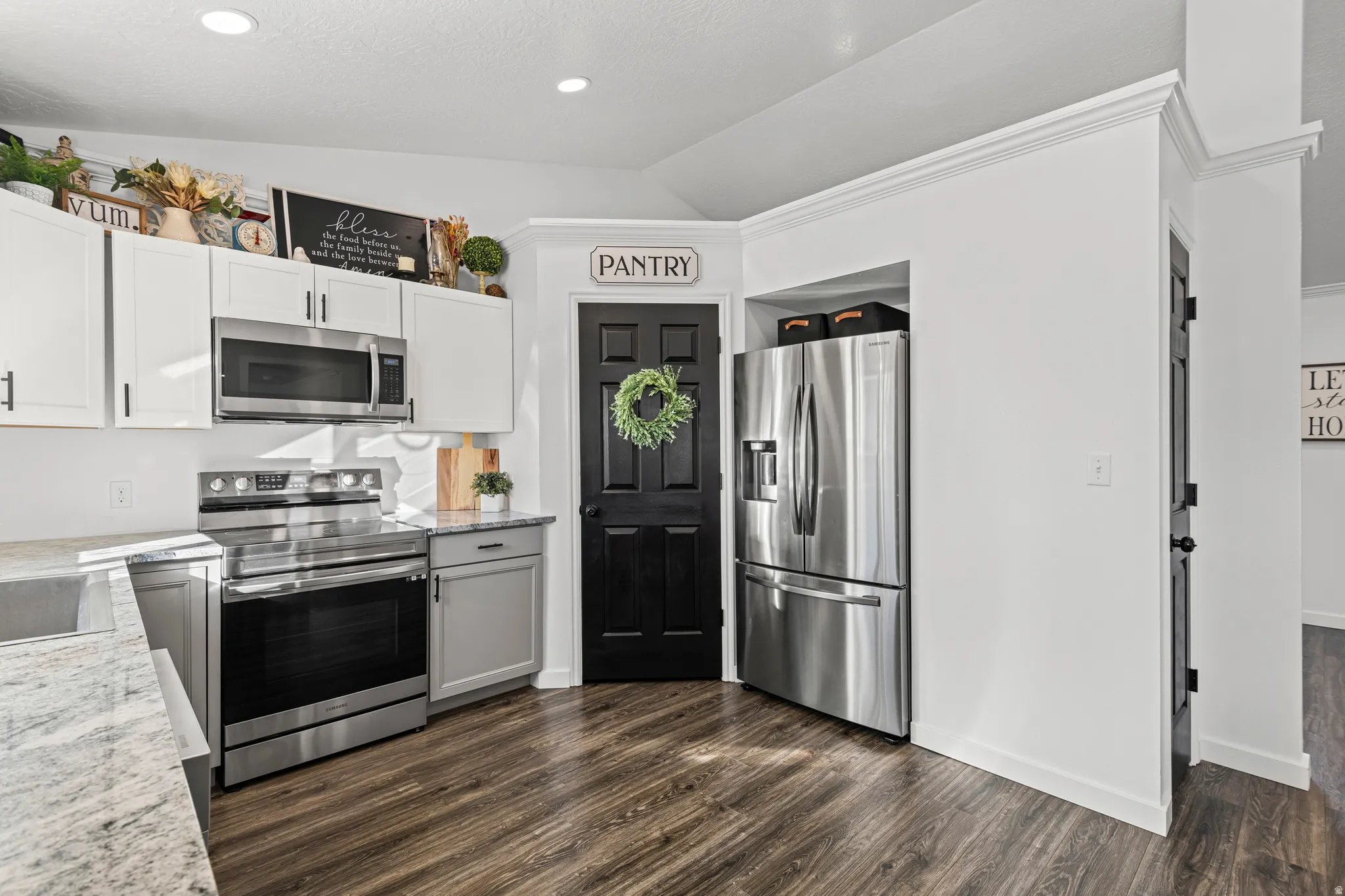 Kitchen featuring stainless steel appliances, vaulted ceiling, light stone countertops, dark wood-type flooring, and two tone color scheme