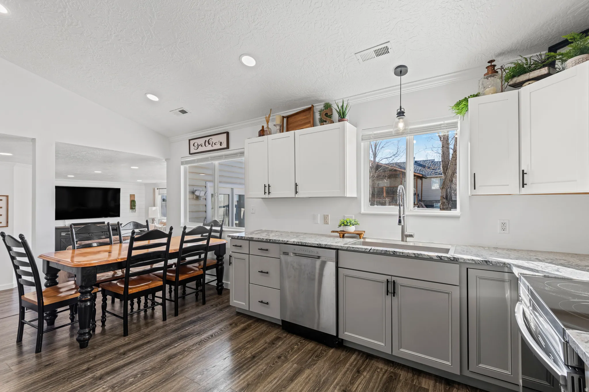 Kitchen with dual tone cabinets, light stone countertops, stainless steel appliances, dark wood-style floors, and hanging light fixtures
