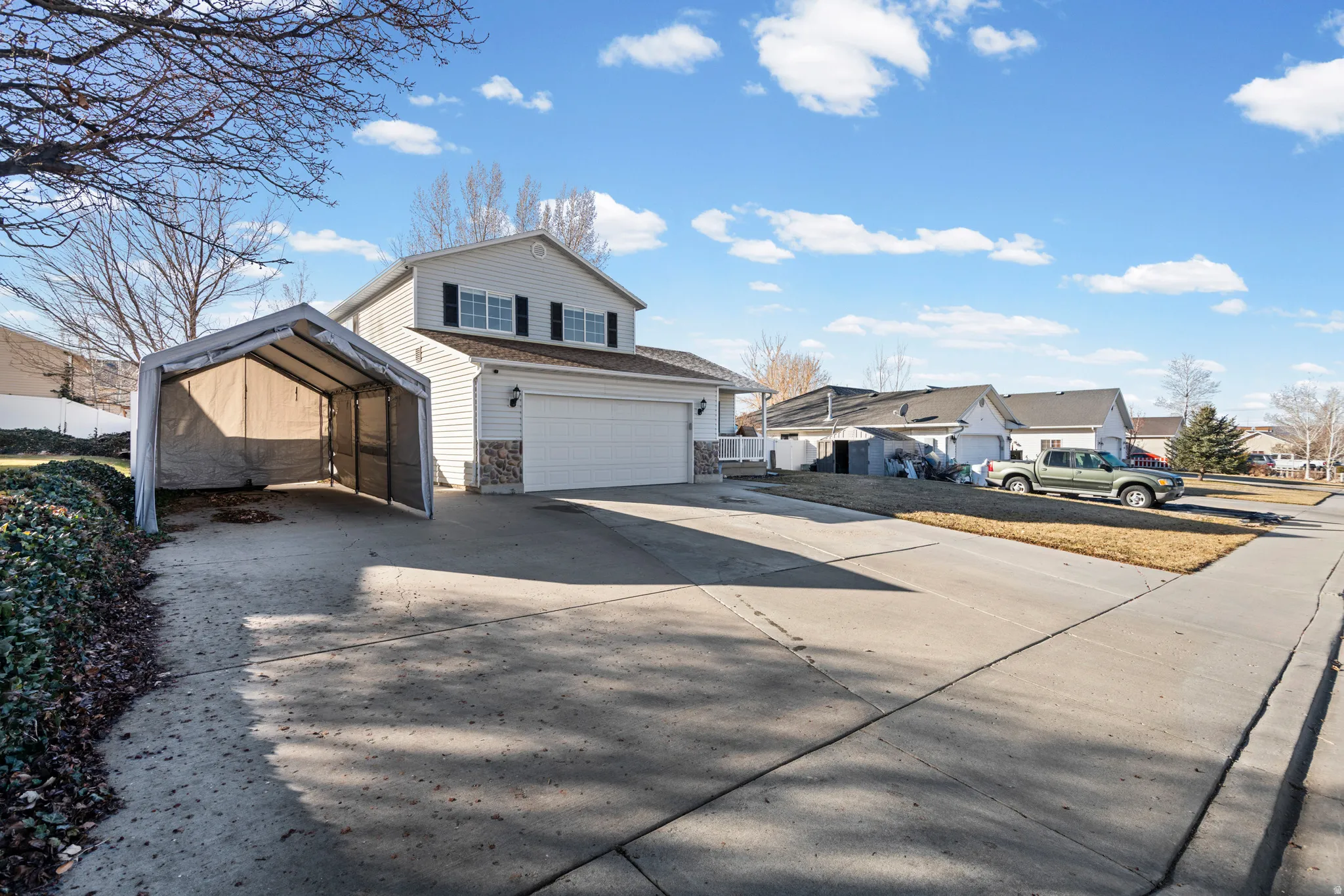 View of front of home featuring concrete driveway, an attached garage, stone siding, a carport, and a residential view
