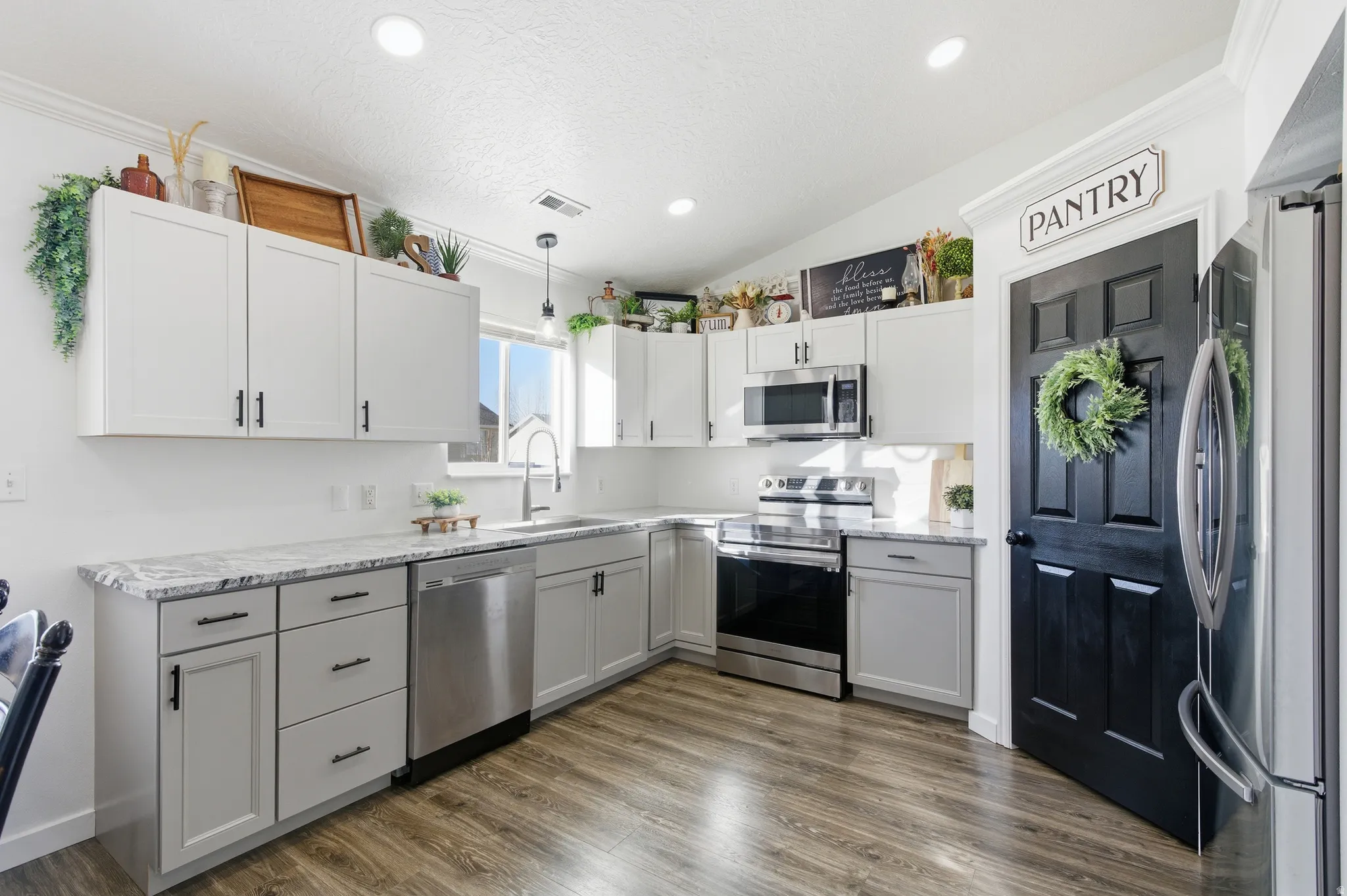 Kitchen with stainless steel appliances, decorative light fixtures, dark wood finished floors, white cabinetry, and lofted ceiling