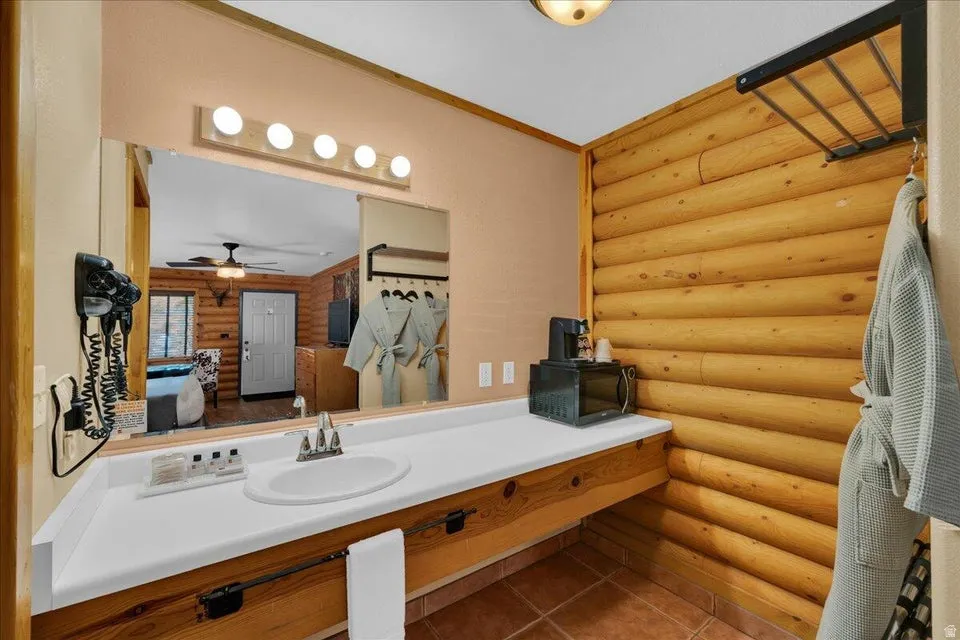 Bathroom featuring rustic walls, vanity, dark tile patterned flooring, ornamental molding, and ensuite bath