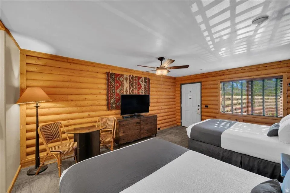 Carpeted bedroom featuring log walls and ceiling fan