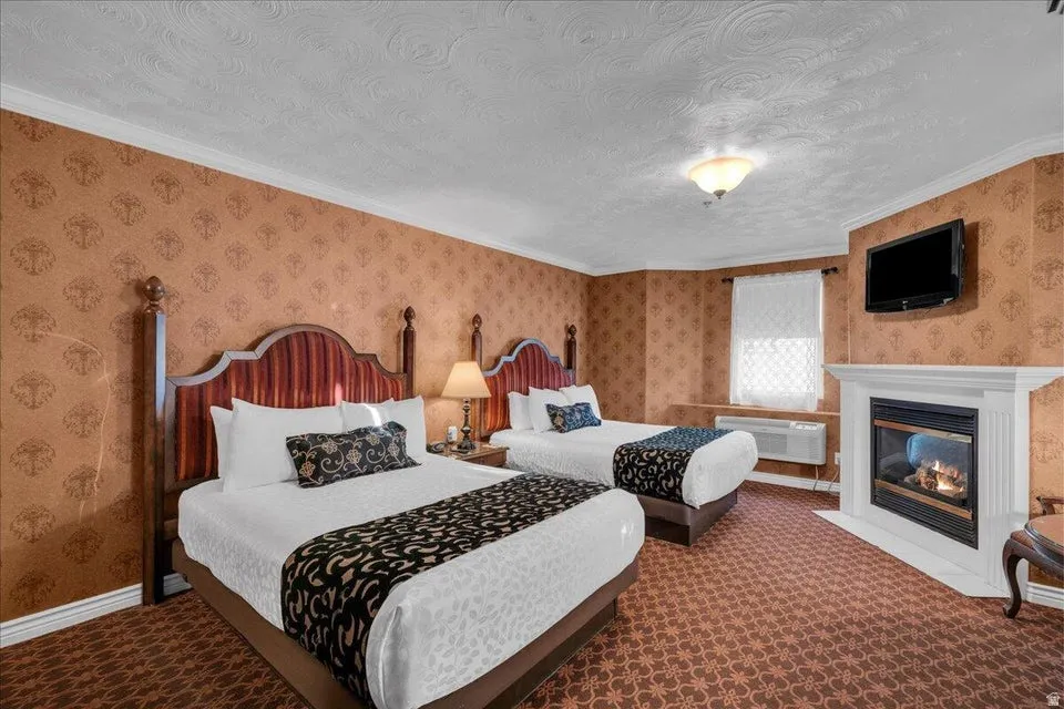 Carpeted bedroom featuring wallpapered walls, ornamental molding, a textured ceiling, and a fireplace with flush hearth