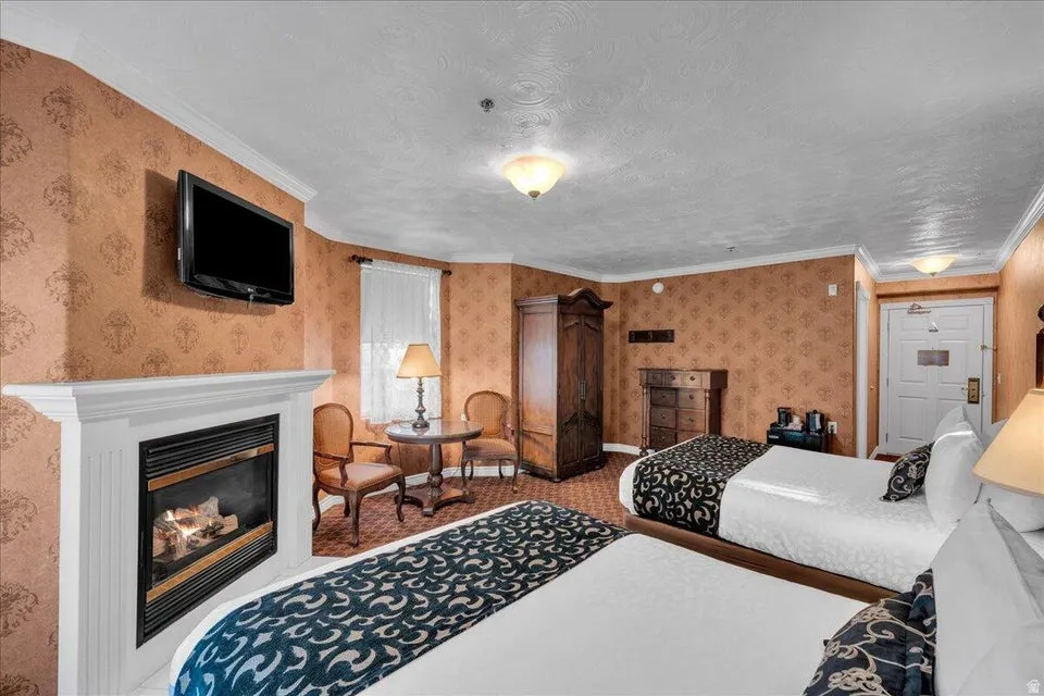 Bedroom with wallpapered walls, crown molding, a glass covered fireplace, and carpet