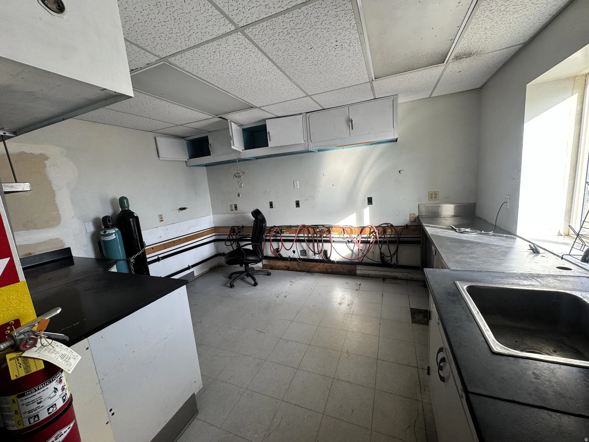 Kitchen with a paneled ceiling, light floors, white cabinets, and dark countertops