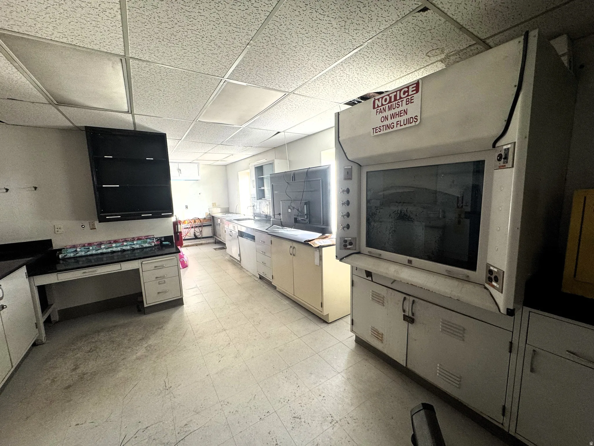 Kitchen with light floors, a drop ceiling, dark countertops, and white cabinets
