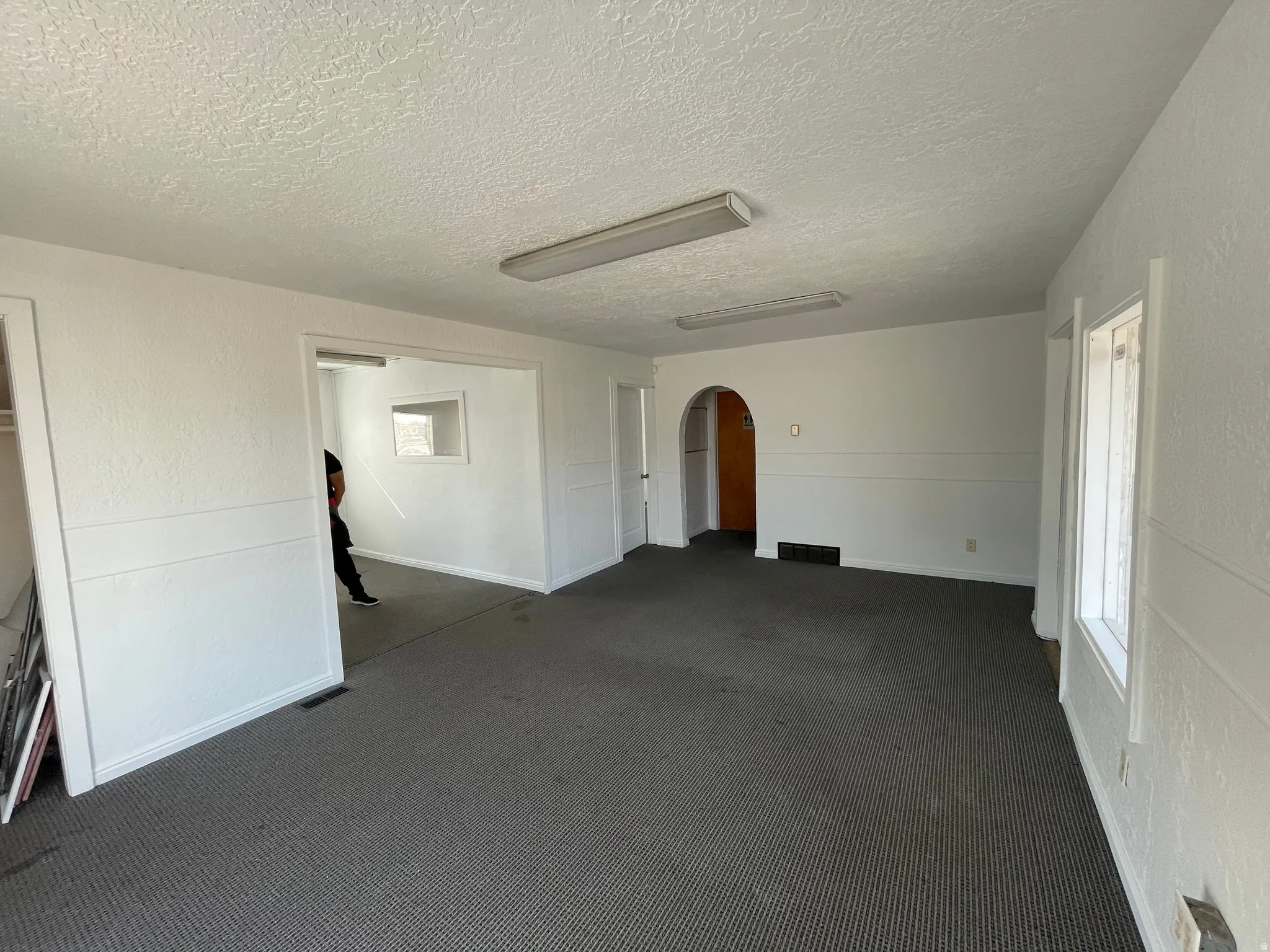 Unfurnished room featuring arched walkways, dark colored carpet, a textured wall, and a textured ceiling