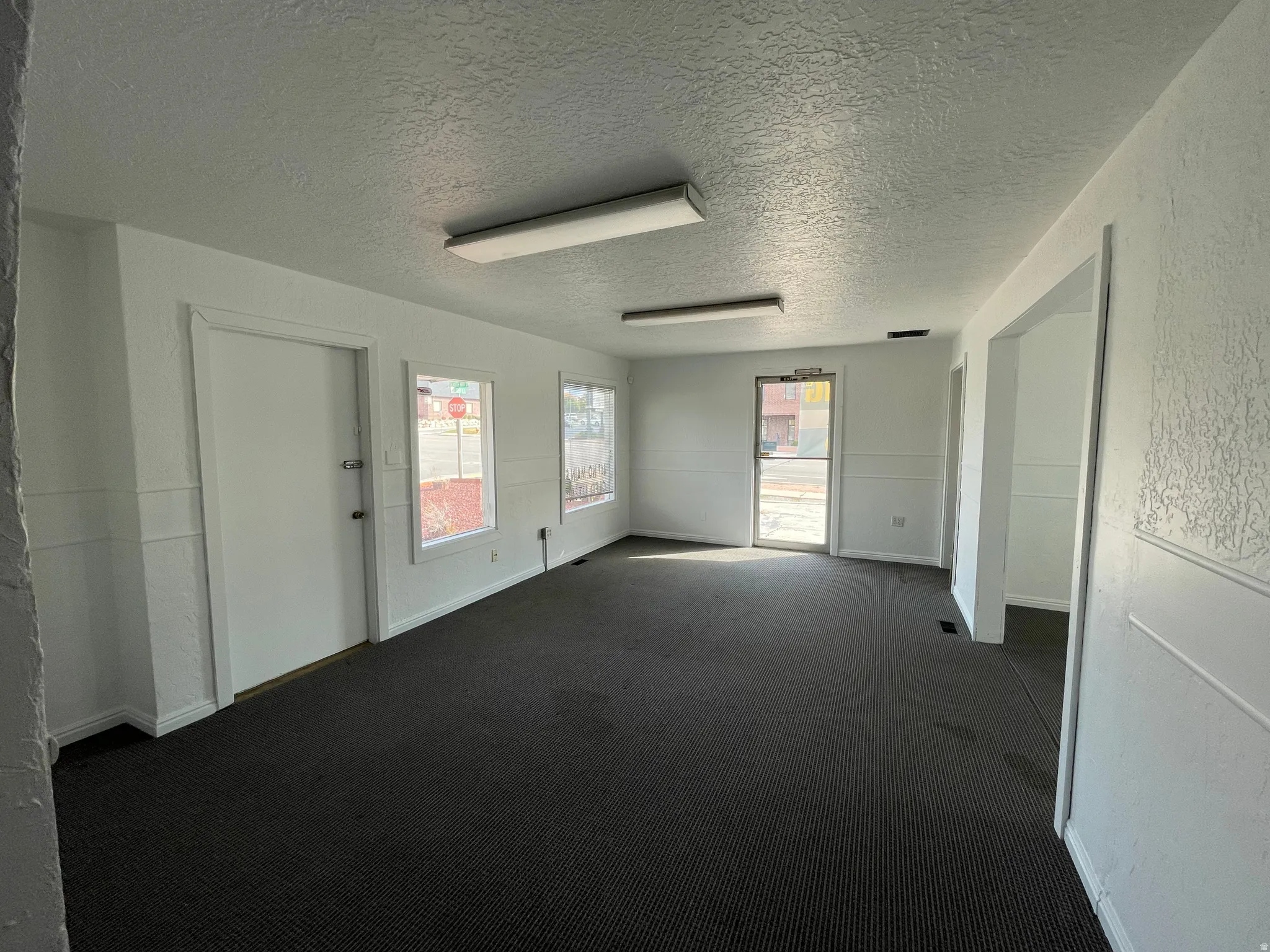 Carpeted empty room featuring a textured ceiling and a textured wall