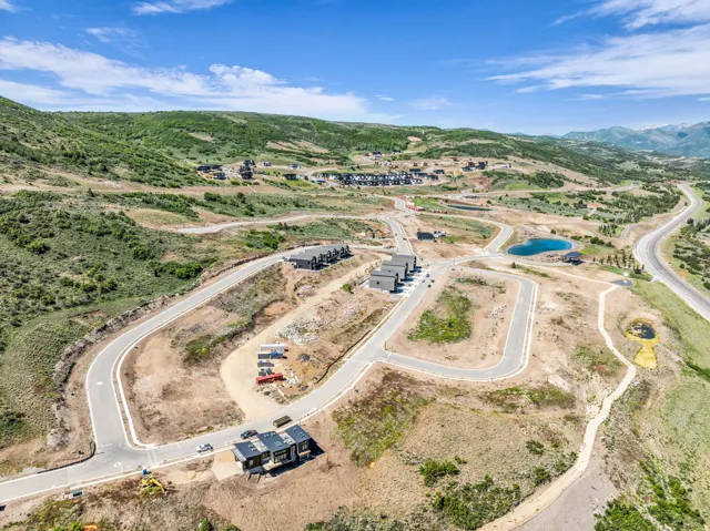 Developing hillside community featuring paved roads, scattered modern residential structures, and natural green landscaping