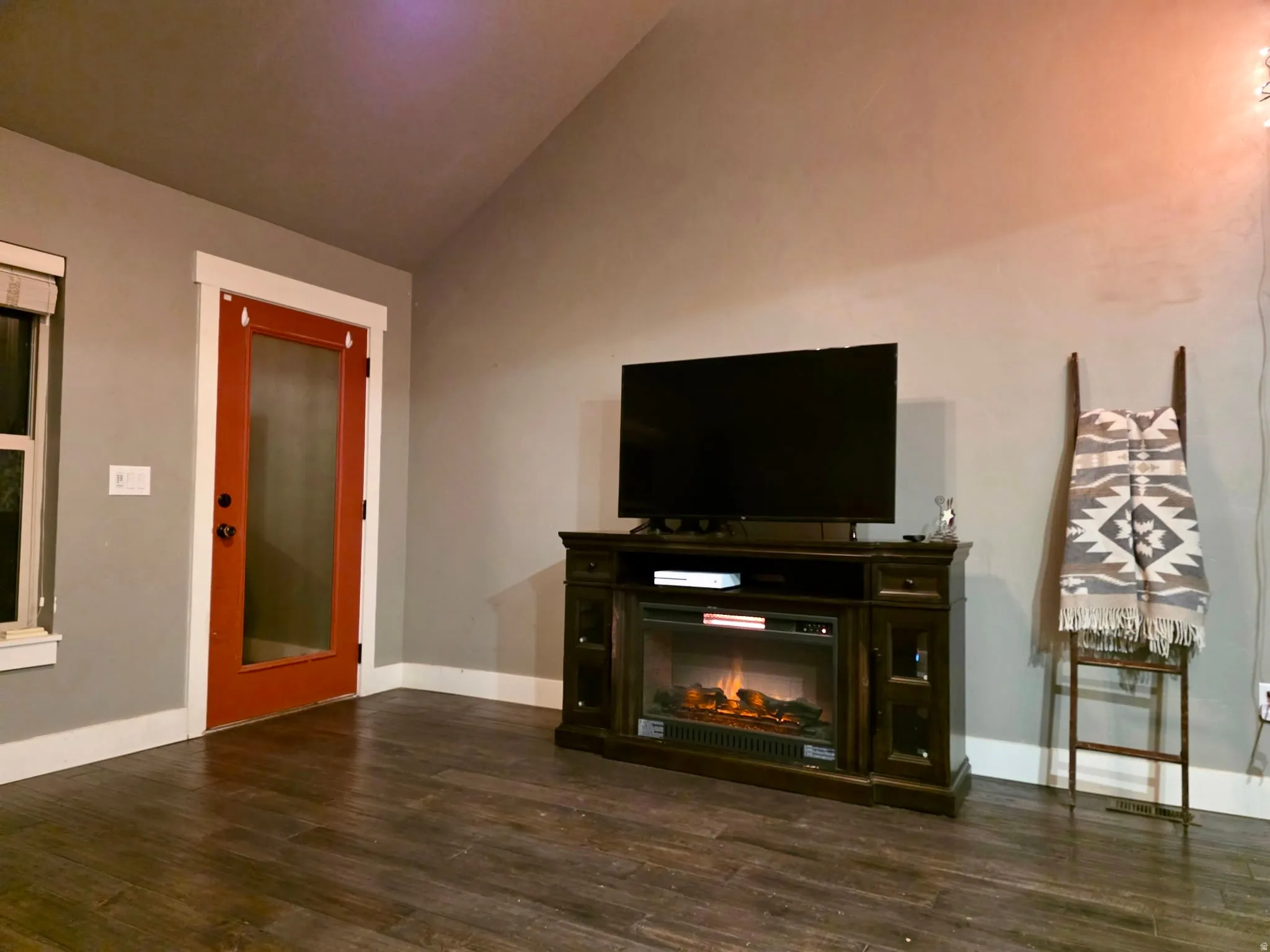 Unfurnished living room featuring dark wood-style floors, lofted ceiling, and a glass covered fireplace