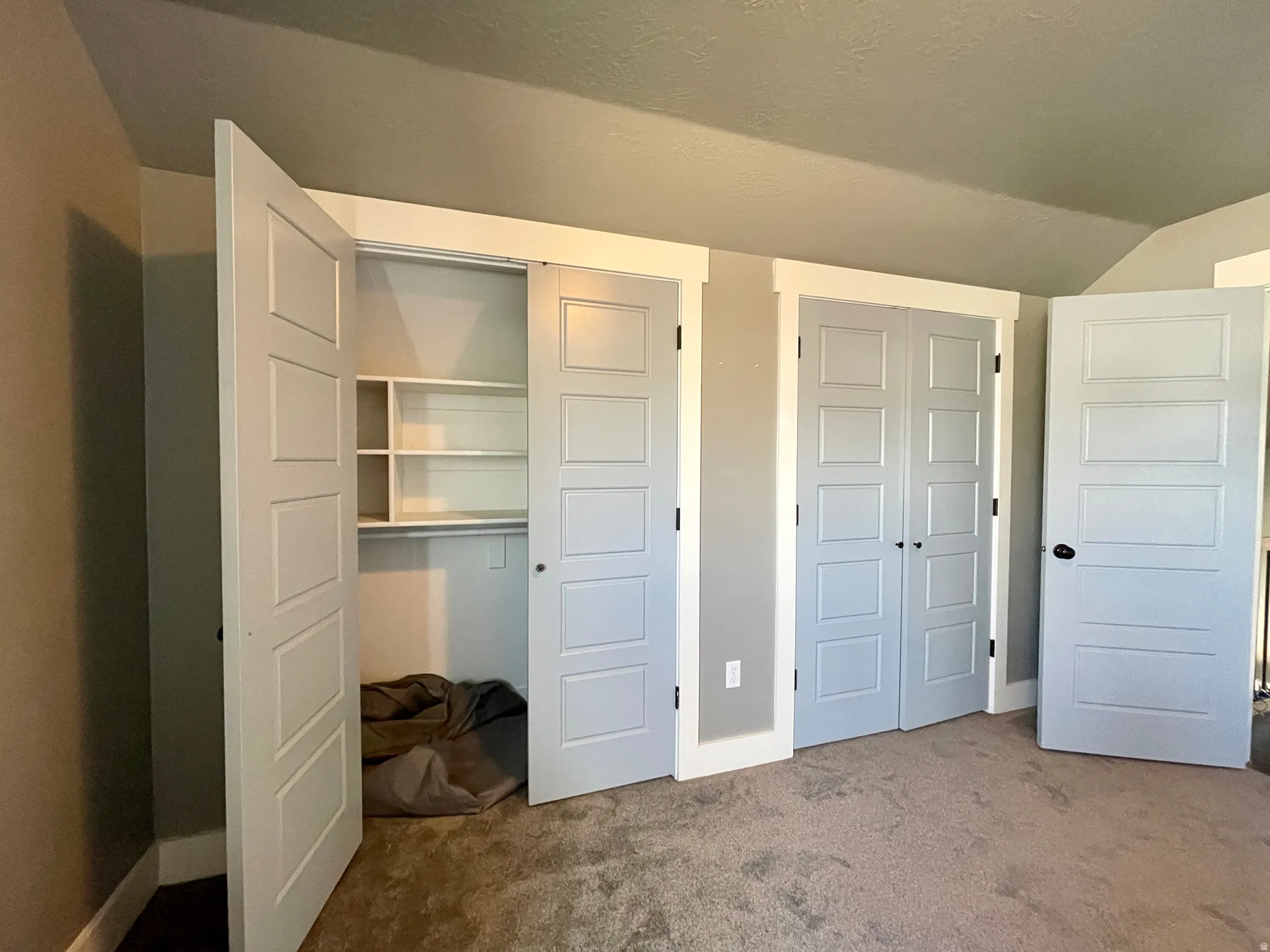 Unfurnished bedroom featuring dark colored carpet and lofted ceiling