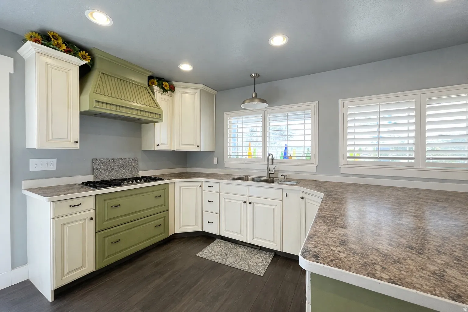 Kitchen with hanging light fixtures, dark wood-style floors, white cabinets, dark countertops, and stainless steel gas cooktop. Edited with AI to show clean space