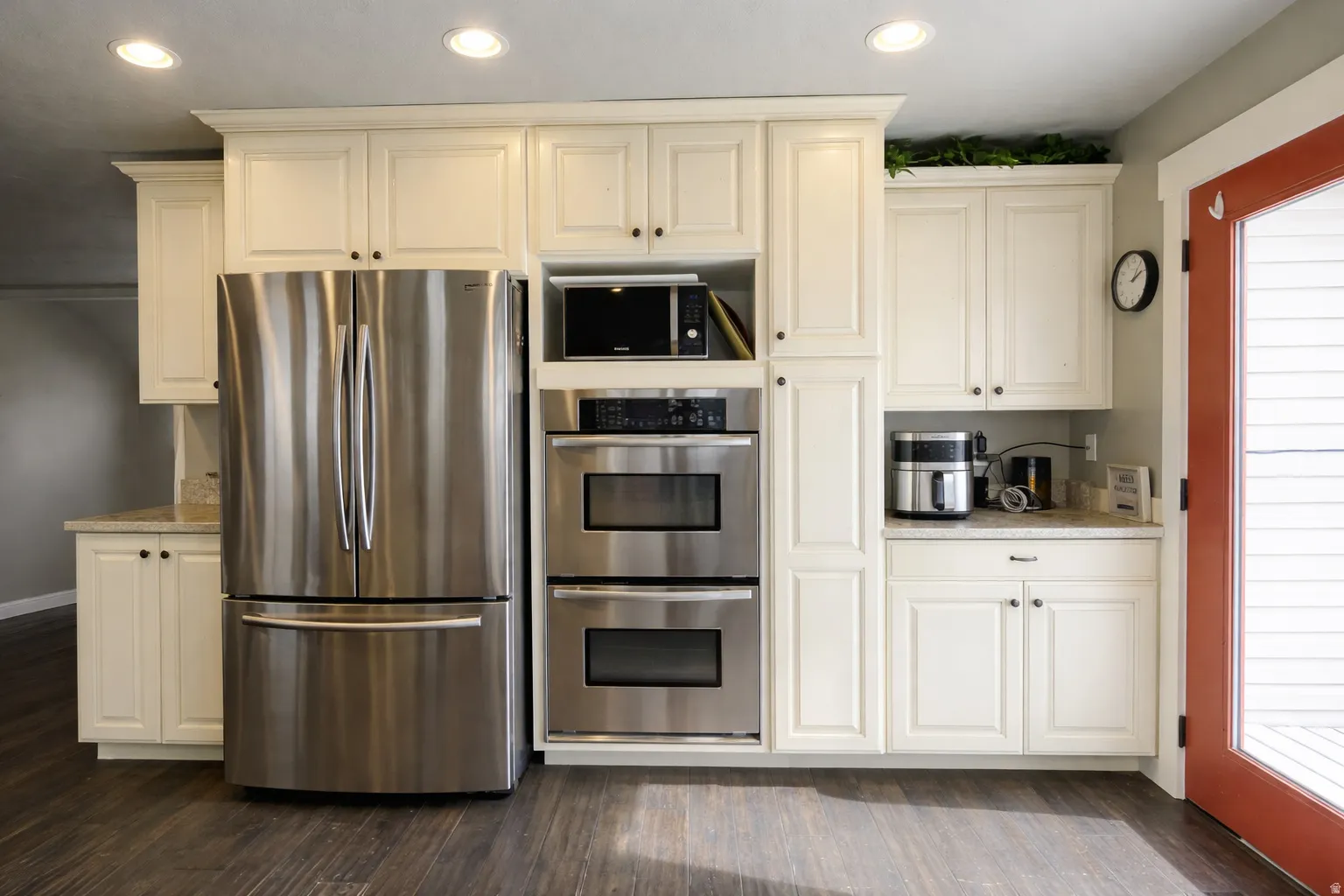 Kitchen with stainless steel appliances, dark wood-style floors, recessed lighting, light stone counters, and white cabinetry. Edited with AI to show clean space