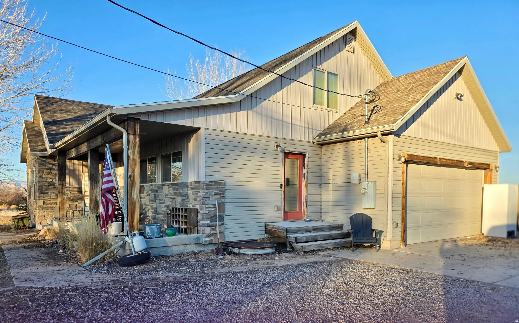 View of front facade with a shingled roof, driveway, stone siding, and a garage