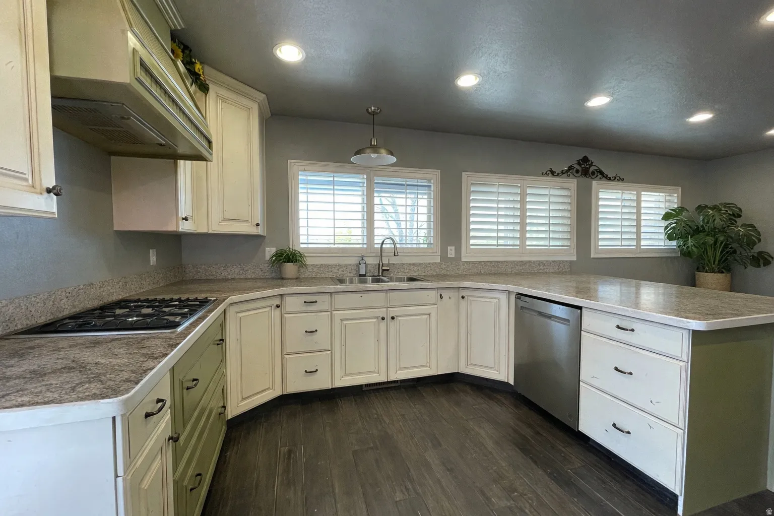 Kitchen with dark wood-style floors, a peninsula, stainless steel appliances, light countertops, and healthy amount of natural light. Edited with AI to show clean space