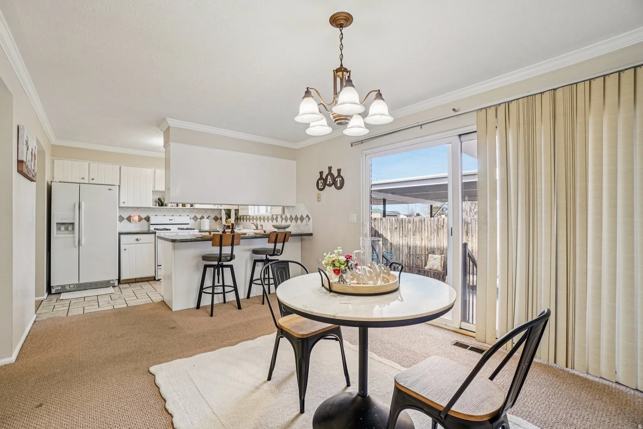 Dining room with light colored carpet, ornamental molding, and a chandelier