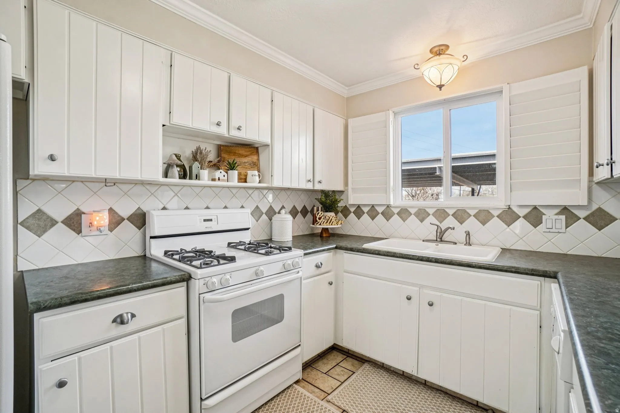 Kitchen with white gas range, dark countertops, white cabinetry, crown molding, and open shelves