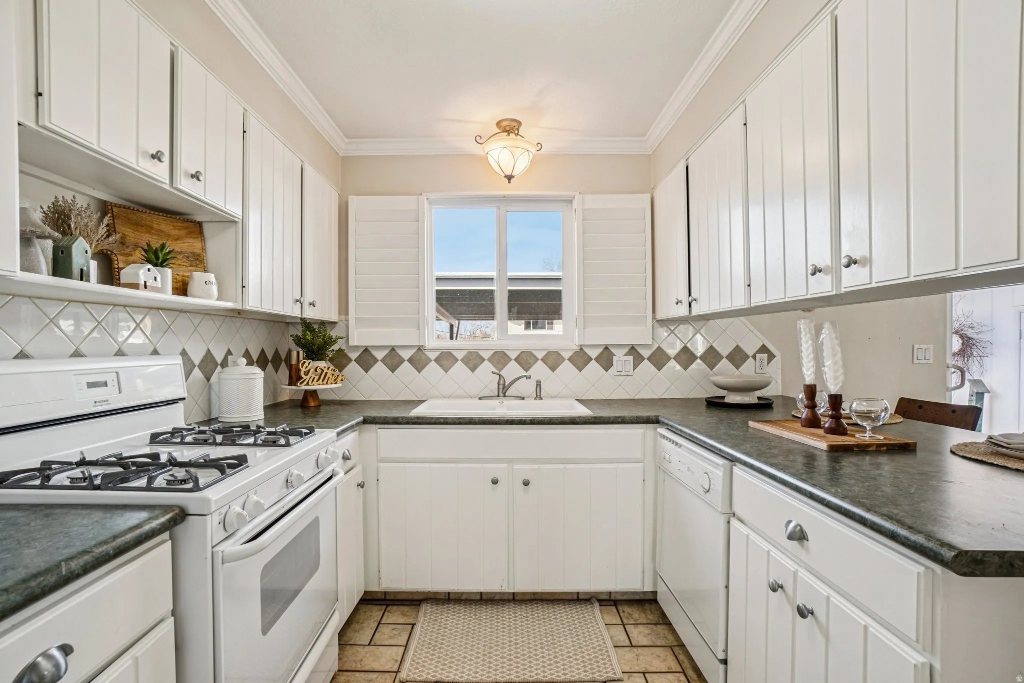 Kitchen with white appliances, white cabinets, dark countertops, a peninsula, and crown molding