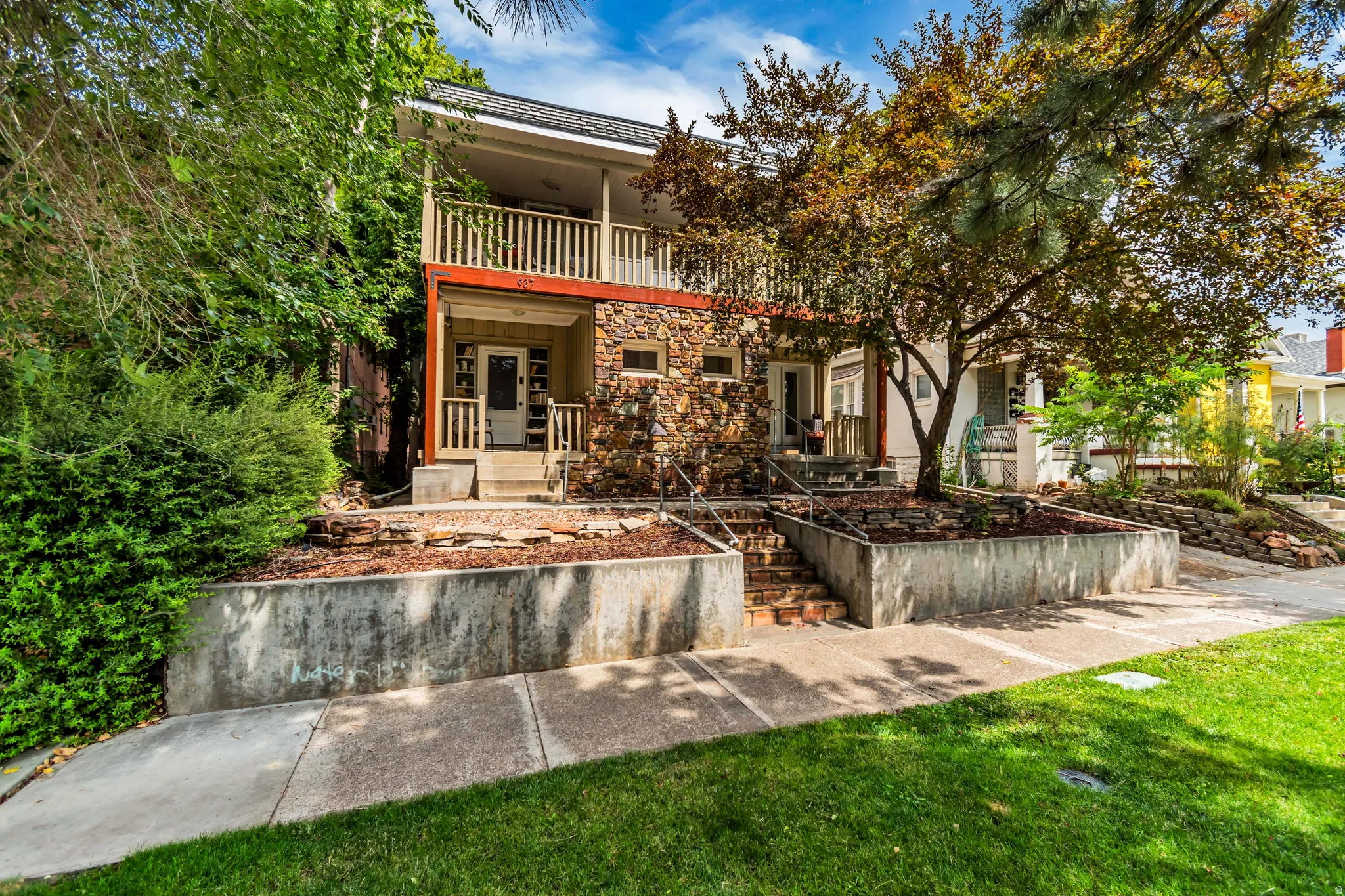 Stone facade with dual-level balconies, concrete retaining walls, and a manicured lawn