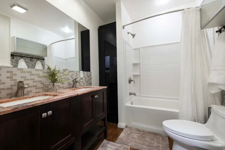 Apt. #1 Bathroom with double vanity, tiled backsplash, and dark wood-style floors