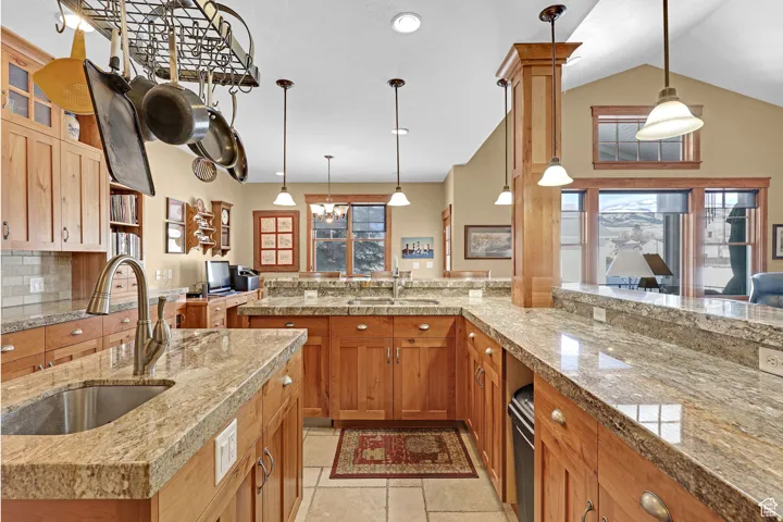 Kitchen featuring hanging light fixtures, brown cabinets, tasteful backsplash, glass insert cabinets, and vaulted ceiling