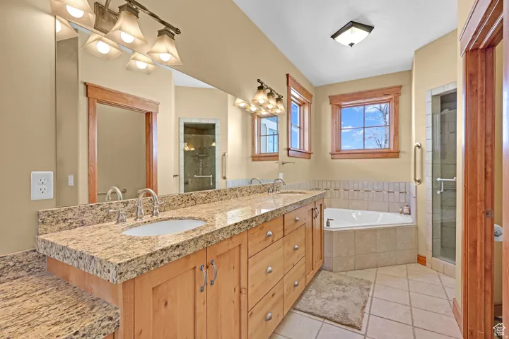 Full bath featuring a shower stall, double vanity, a bath, and light tile patterned flooring