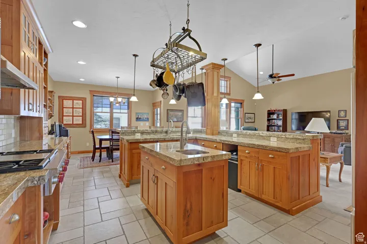 Kitchen featuring brown cabinetry, open floor plan, gas range, pendant lighting, and high vaulted ceiling