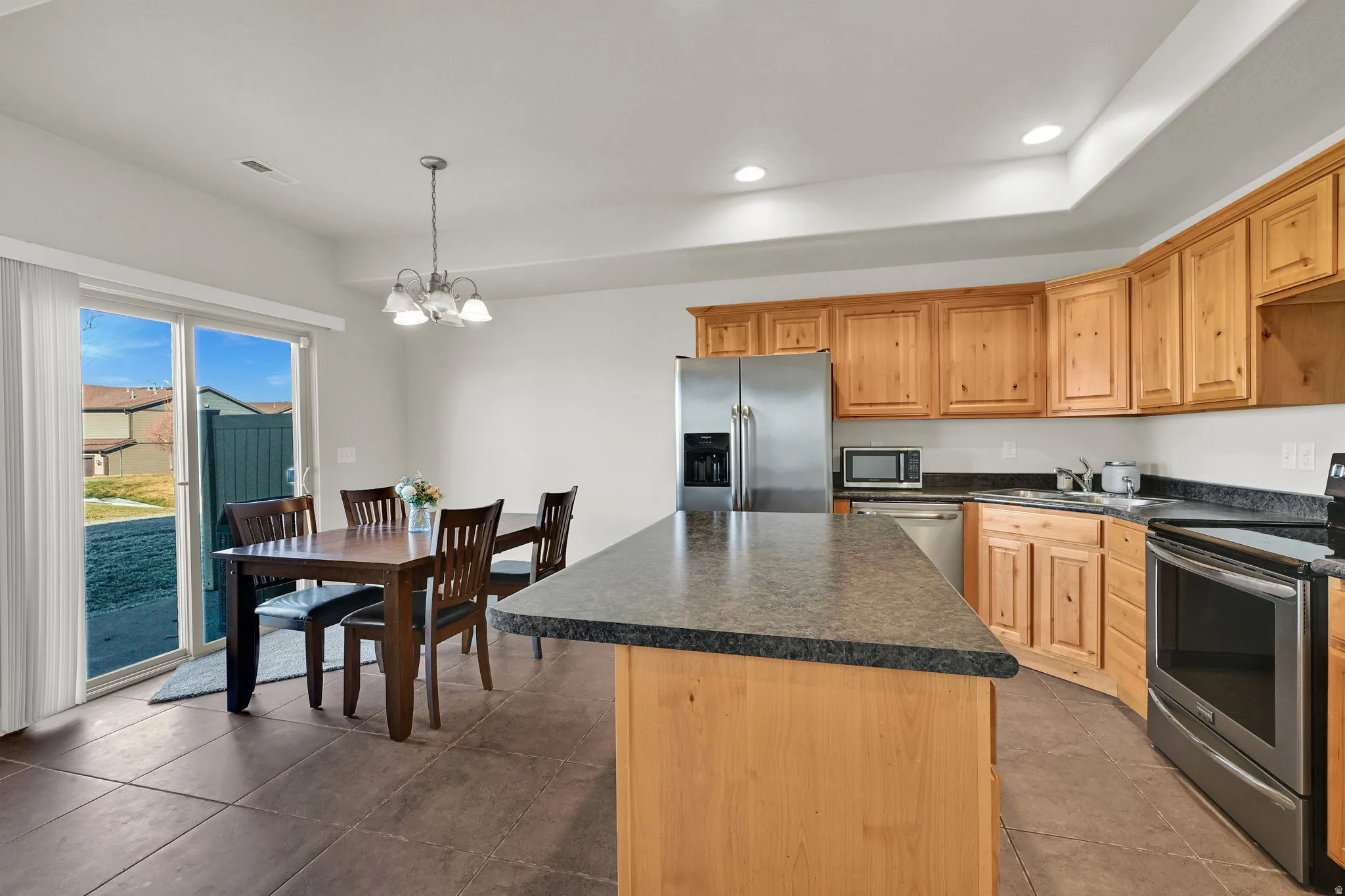 Kitchen featuring stainless steel appliances, a center island, suspended lighting, dark countertops, and dark tile patterned flooring