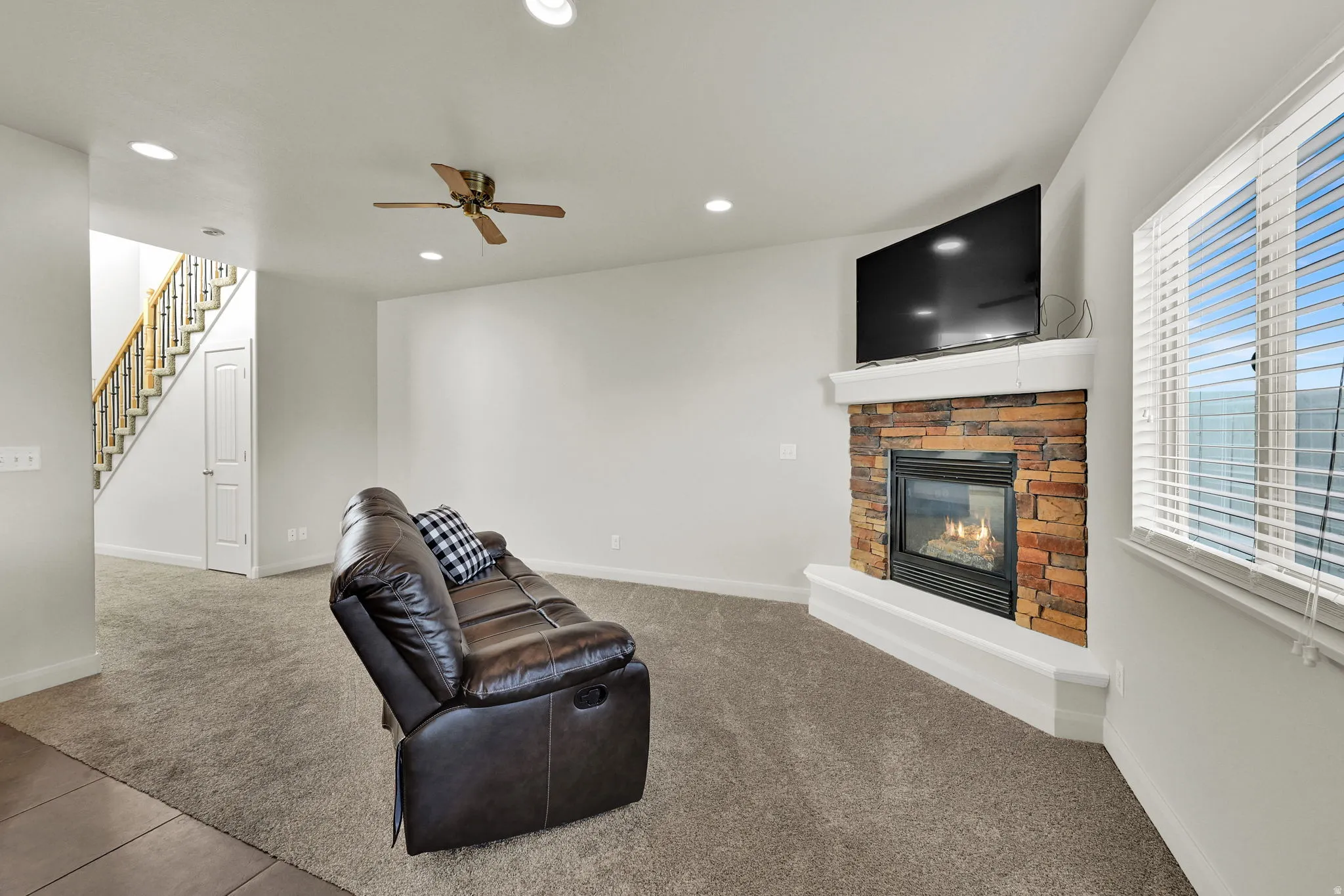 Unfurnished living room featuring light colored carpet, a stone fireplace, recessed lighting, and ceiling fan