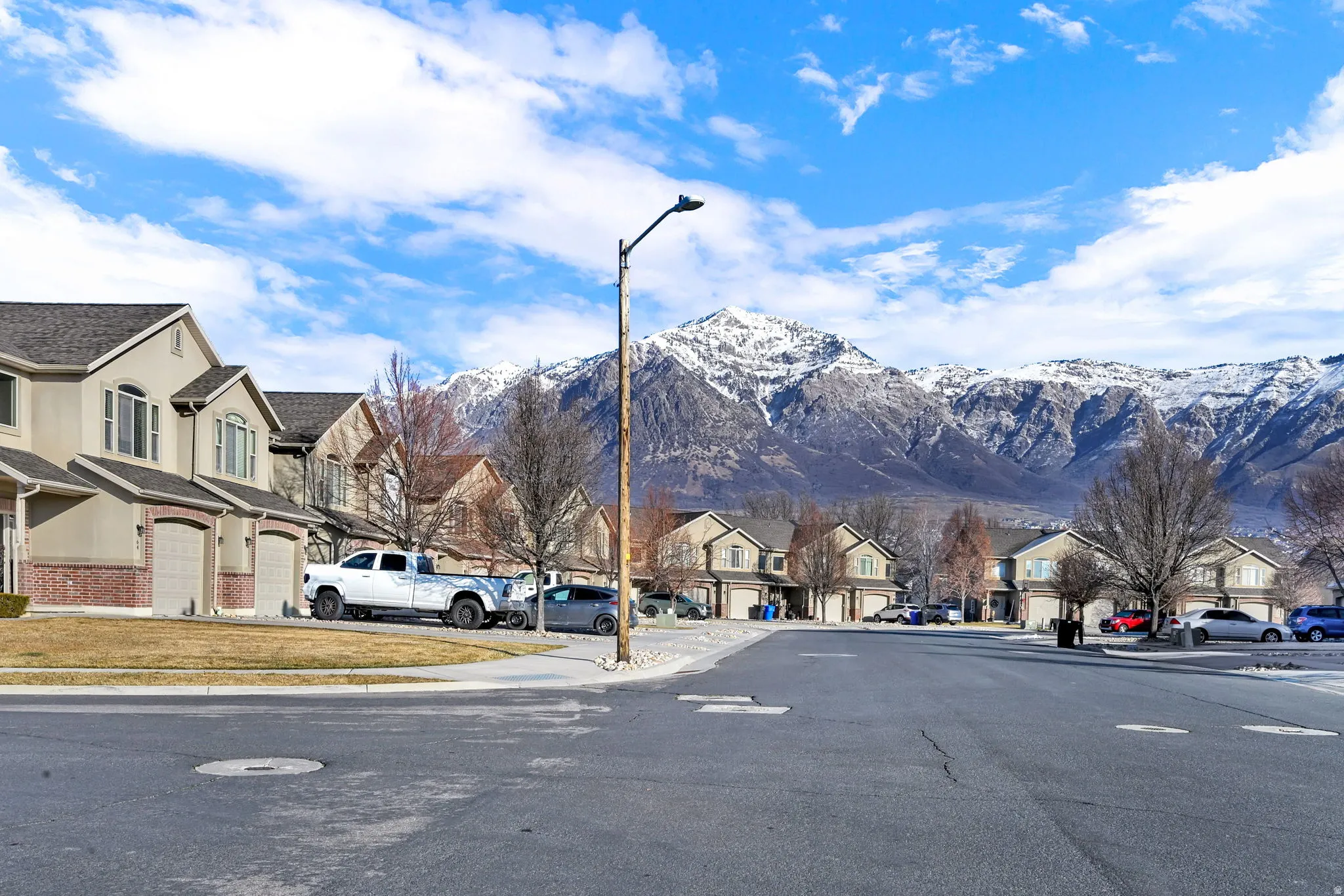 View of asphalt street with sidewalks, a residential view, street lighting, a mountain view, and curbs